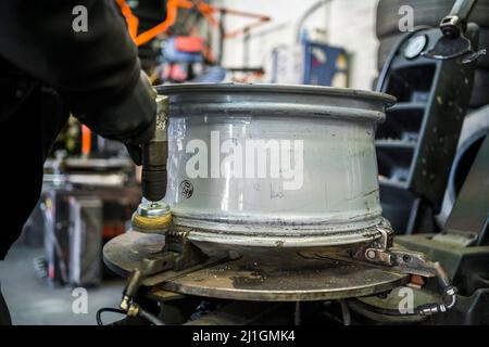 Tyre garage workshop. Garage staff clean the inside rim of an alloy wheel with an electric metal brush prior to tyre fitting. Stock Photo