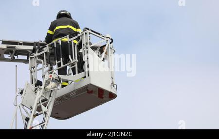 brave firefighter who saves the injured person using the truck with the ladder truck during an emergency and sky on background Stock Photo