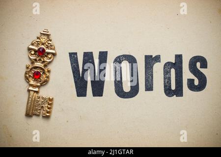 Golden key next to 'Words' written on yellowed vintage paper texture. Creative concept representing keywords Stock Photo