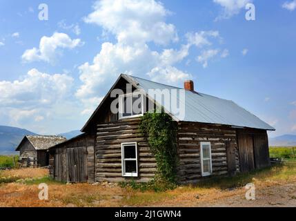Rustic log cabin still stands as evidence of the early residents of Happy Valley, Montana.  Gallatin Mountains are in distance. Stock Photo