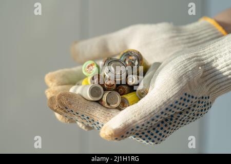 Close up of female hands in cotton protection gloves holding used alkaline batteries heap Stock Photo