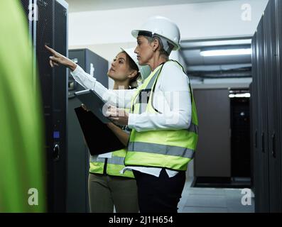 Learning on the job. Cropped shot of two attractive female programmers working in a server room. Stock Photo