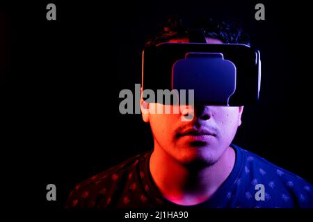 Young latin man using Virtual Reality VR Headset 3D Glasses. Dark backdrop. Low key. Copy space. Stock Photo