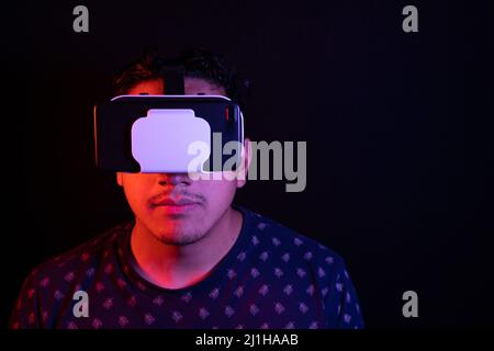Young latin man using Virtual Reality VR Headset 3D Glasses. Dark backdrop. Low key. Copy space. Stock Photo
