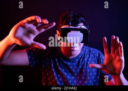Young latin man using Virtual Reality VR Headset 3D Glasses and trying to hold something with his hands. Dark backdrop. Stock Photo