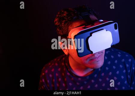 Young latin man using Virtual Reality VR Headset 3D Glasses. Dark backdrop. Low key. Copy space. Stock Photo
