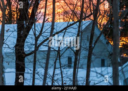 Beautiful orange sunset over snow covered house in woods Stock Photo