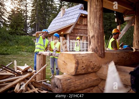 Young smiling constructer couple chatting on construction site. Other workers working in the background. Wooden Skeleton Framing Building. Constructio Stock Photo