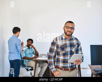 Smart technology makes management so much simpler. Portrait of a young entrepreneur using a digital tablet at work with his team in the background. Stock Photo