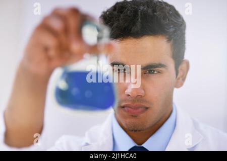 Scrutinizing samples. Shot of a lab technician examining a beaker of blue liquid while standing in a lab. Stock Photo