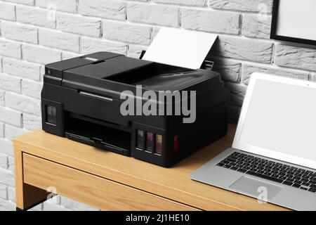 Modern printer and laptop on table near grey brick wall Stock Photo