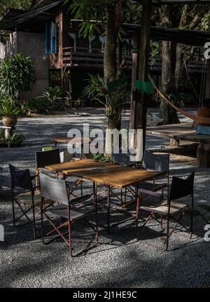 Wooden old table and Empty folding camping chairs in front of the house with nature environment with morning sun rays shine through. Selective focus. Stock Photo