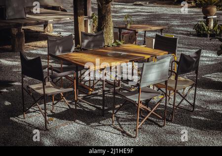 Wooden old table and Empty folding camping chairs in front of the house with nature environment with morning sun rays shine through. Selective focus. Stock Photo