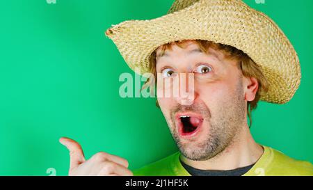 Portrait of a shocked guy in a yellow shirt stands on green background and points his finger away at copy space. A surprised charismatic young man loo Stock Photo