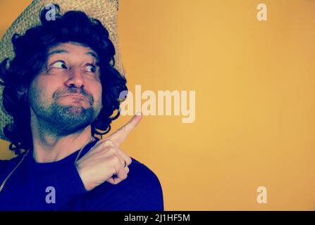 Happy hispanic funny young bearded man wearing a hat pointing aside with fingers hand gesture at copy space advertising new promotion, presenting sale Stock Photo