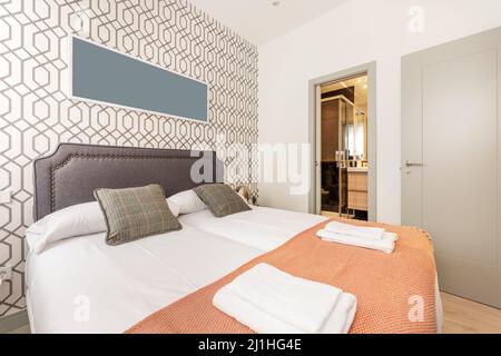 bedroom with double beds with white bedding, green cushions, studded gray leather upholstered headboard, tile-colored blanket and access to an en-suit Stock Photo