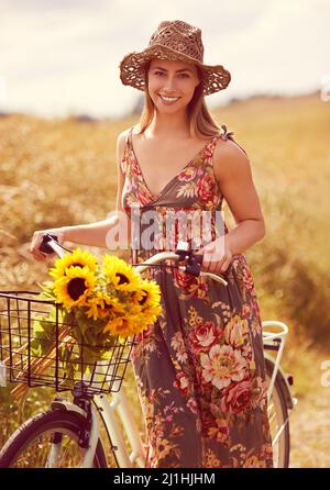 All she needs is a bike and the great outdoors. Shot of a young woman cycling through the countryside with a bunch of sunflowers. Stock Photo