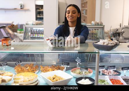 Smiling young female caucasian employee holding bowl on cabinet in coffee shop. unaltered, cafe culture, people and occupation concept. Stock Photo
