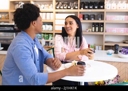 Happy young multiracial couple talking while sitting with coffee at table in cafe. unaltered, cafe culture, people, love and lifestyle concept. Stock Photo