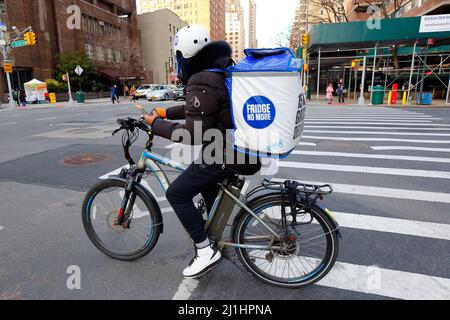 A Fridge No More delivery person on an e bike holds a smartphone with map directions while pausing at a New York City intersection, March 3, 2022. Stock Photo