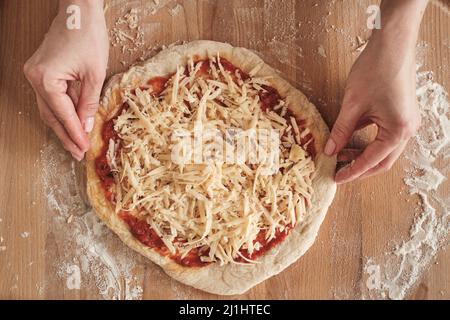 High angle view of female hands adjusting shape of pizza dough while preparing pizza for baking Stock Photo