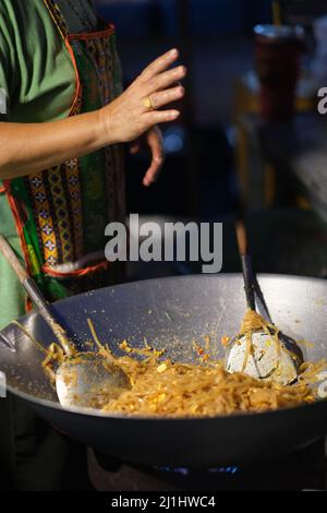 A woman is cooking a pad thai on a stall at a night market in Bangkok, Thailand Stock Photo