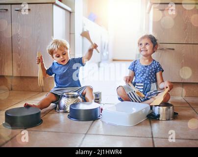 Lets make some noise. Shot of two adorable children playing on a drum set made of pots on the kitchen floor. Stock Photo