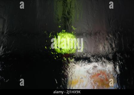 Water is flowing down over window, with blurred colorful lights behind Stock Photo