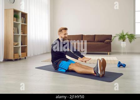 Athletic man at home doing sports stretching stretching his arms to tips of his legs. Stock Photo