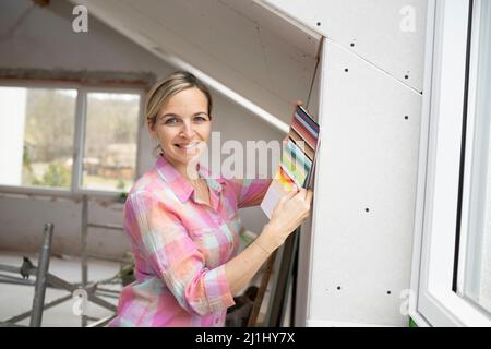 Interior designer with colorful blouse works on construction site in a house loft with color cards Stock Photo