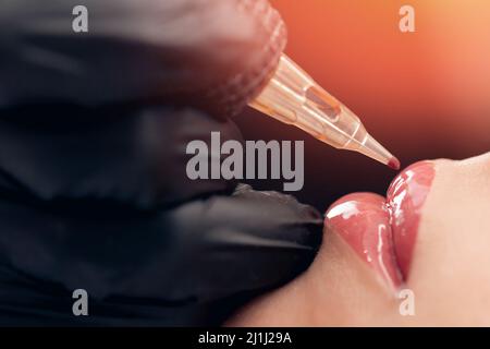 Macro photo of process of applying permanent makeup tattoo of red on lips woman. Stock Photo