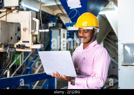 engineer in uniform busy working on laptop at machinery in factory - concept of technology, skilled or professional labour and development. Stock Photo