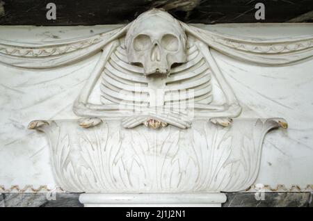 A marble carving from the 18th century showing a skeleton resting his folded arms on a plinth decorated with acanthus leaves.  On a memorial plaque wh Stock Photo