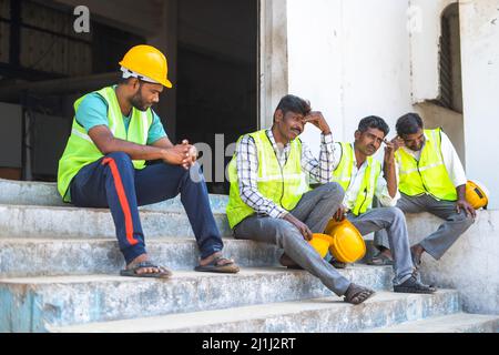 worried industrial workers sitting outside the factory due to closure - concept of job loss, unemployment and blue collar jobs Stock Photo