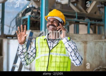 smiling industrial worker talking on mobile phone with family at factory - concept of communication, taking break, relaxed and technology. Stock Photo
