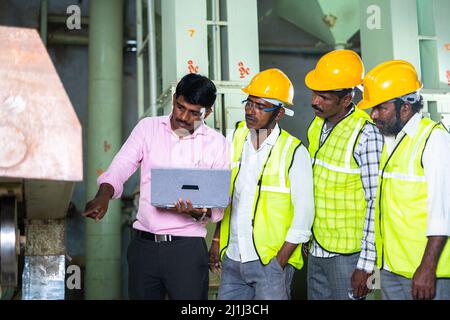 supervisor explaining about machinery or debugging using laptop while in front of workers - concept of teamwork, skilled workforce and empployee Stock Photo