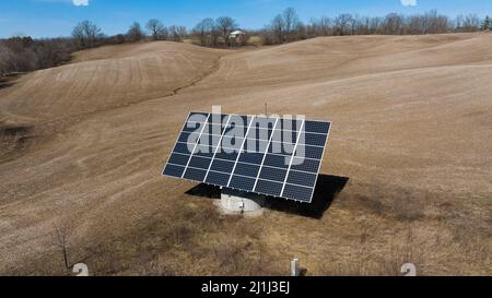 A low aerial view of a large solar tracker in a rural field is seen on a clear, sunny day.