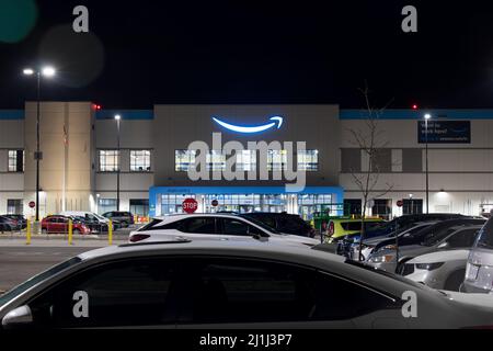 The Amazon logo shines brightly in blue at the top of the front entrance to a large, new fulfillment center near an airport. Stock Photo