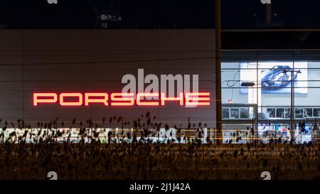 The Porsche text logo on the side of a dealership building is seen while lit in bright red at night. Stock Photo