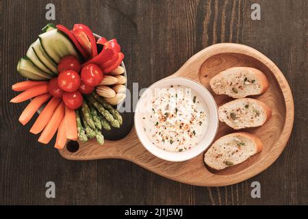 Directly above view of healthy vegetable snacks and baguette slices with white sauce on wooden dining table Stock Photo