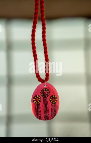 A vertical closeup shot of a necklace made of red stone and thread on the blurry background Stock Photo