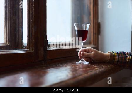 A young man drinks red wine from a vintage glass in an old mansion. Front view. Stock Photo