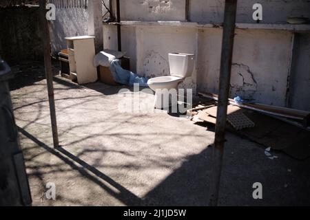 garbage from one old blue dirty toilet bowl lies on brown ground outside Stock Photo