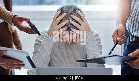 Just give me a break. Shot of a mature businesswoman sitting in the office and feeling stressed while colleagues overwhelm her with tasks. Stock Photo