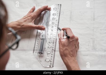 Over shoulder view of female architect or engineer drawing blueprint using ruler and pencil Stock Photo