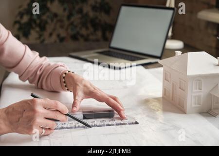 Close-up of unrecognizable female architectural drafter in ring using ruler while working with blueprint of house Stock Photo