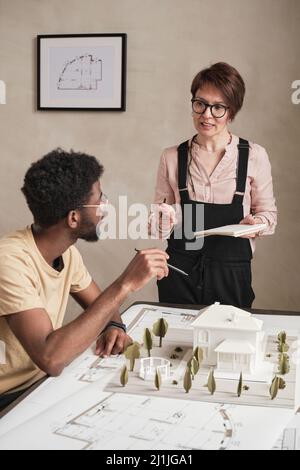 Interracial architects in glasses discussing house structure while working with real estate prototype Stock Photo