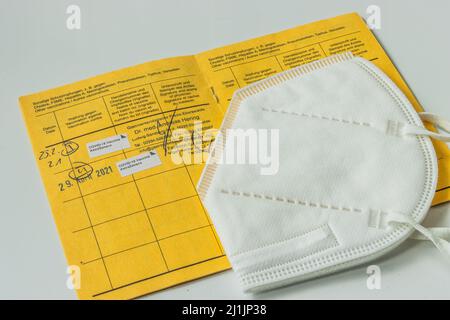 Opened international vaccination card with a white face mask. Entry of two vaccinations against the coronavirus. Page from the yellow vaccination Stock Photo