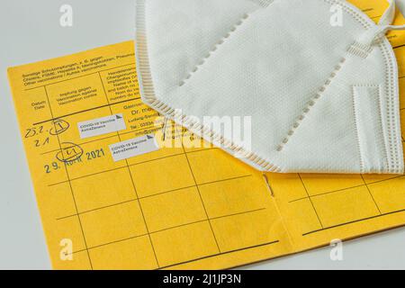 Yellow international vaccination card and white face mask. Registration of the double vaccination against the coronavirus. Page from the yellow vaccin Stock Photo