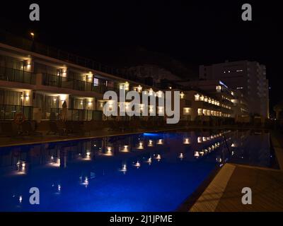 View of the blue shimmering swimming pool of holiday resort in Puerto Rico, southern Gran Canaria, Spain at night with lights reflected in the water. Stock Photo